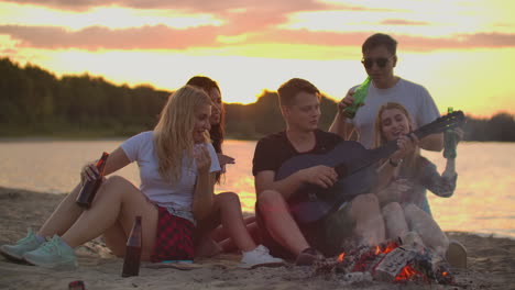 The-five-students-play-the-guitar-and-sing-songs-around-bonfire-on-the-beach-party.-This-is-soulful-summer-evening-with-the-best-friends-and-beer.
